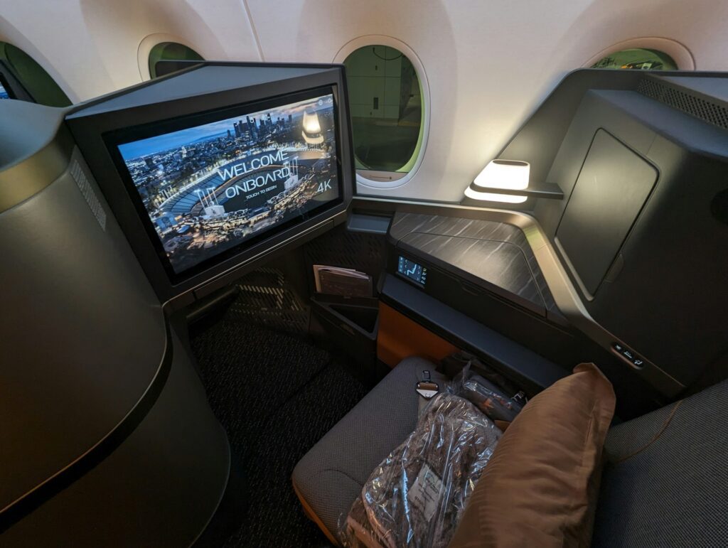 A luxury airplane cabin suite featuring a large entertainment screen, a lie-flat seat, and a private side table
